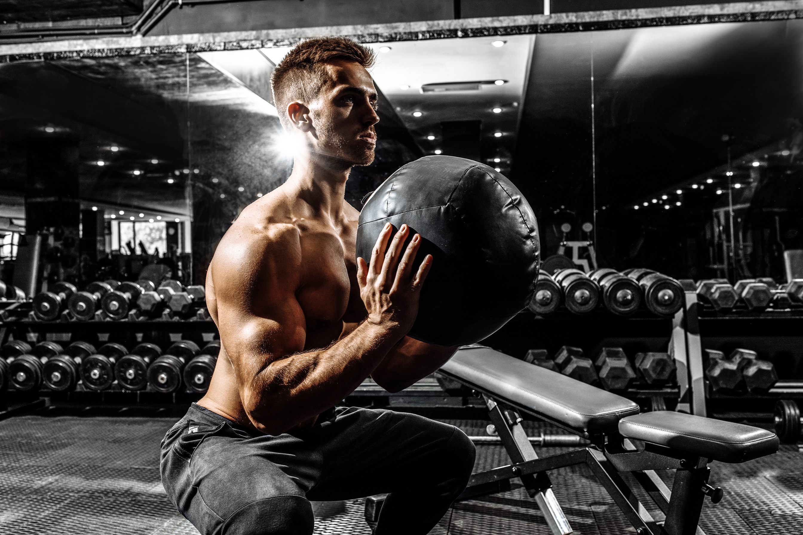 Sporty Man Doing Squats While Holding Ball, Man Doing Medicine Ball Workout in the Gym