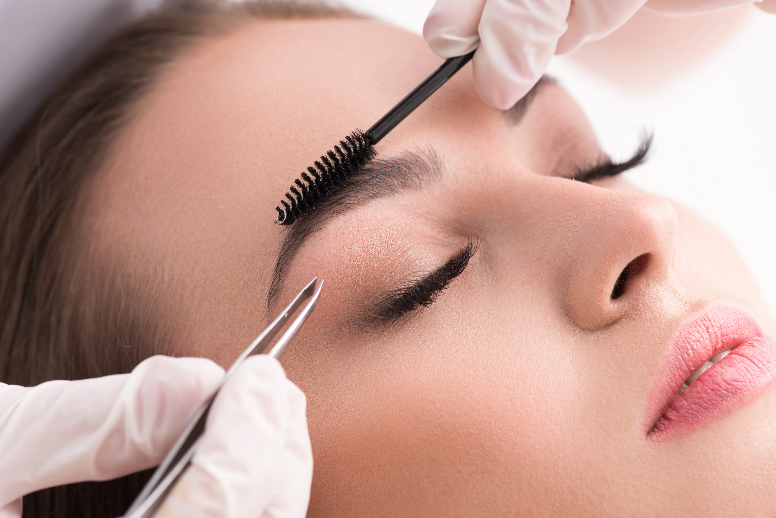 Young woman tweezing her eyebrows in beauty saloon