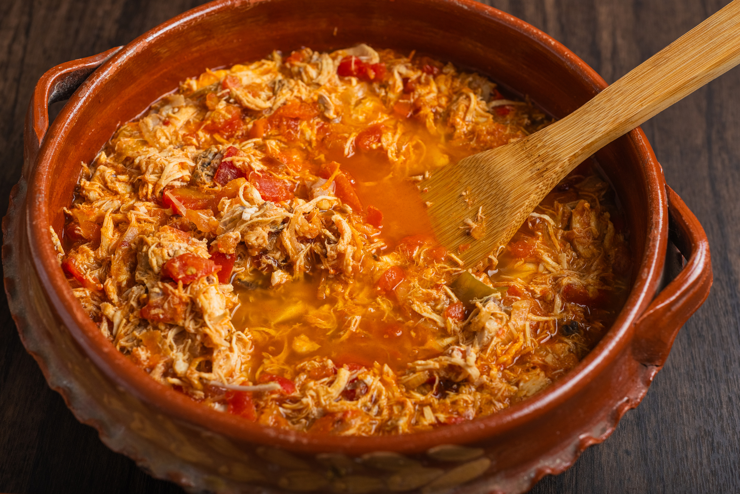 Authentic mexican chicken tinga, typical mexican food prepared in a clay pot on a wooden table.