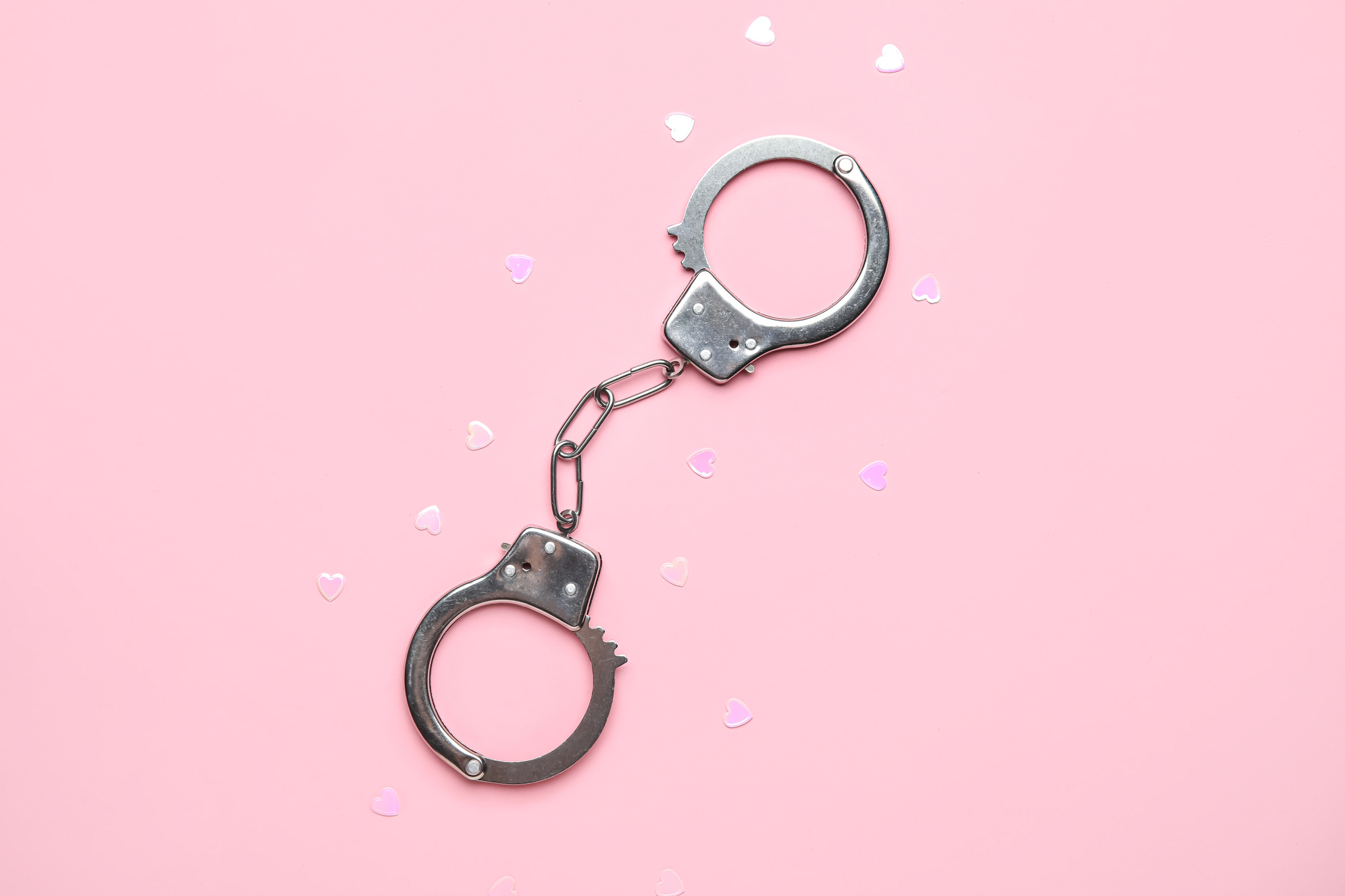 Handcuffs from Sex Shop and Hearts on Pink Background